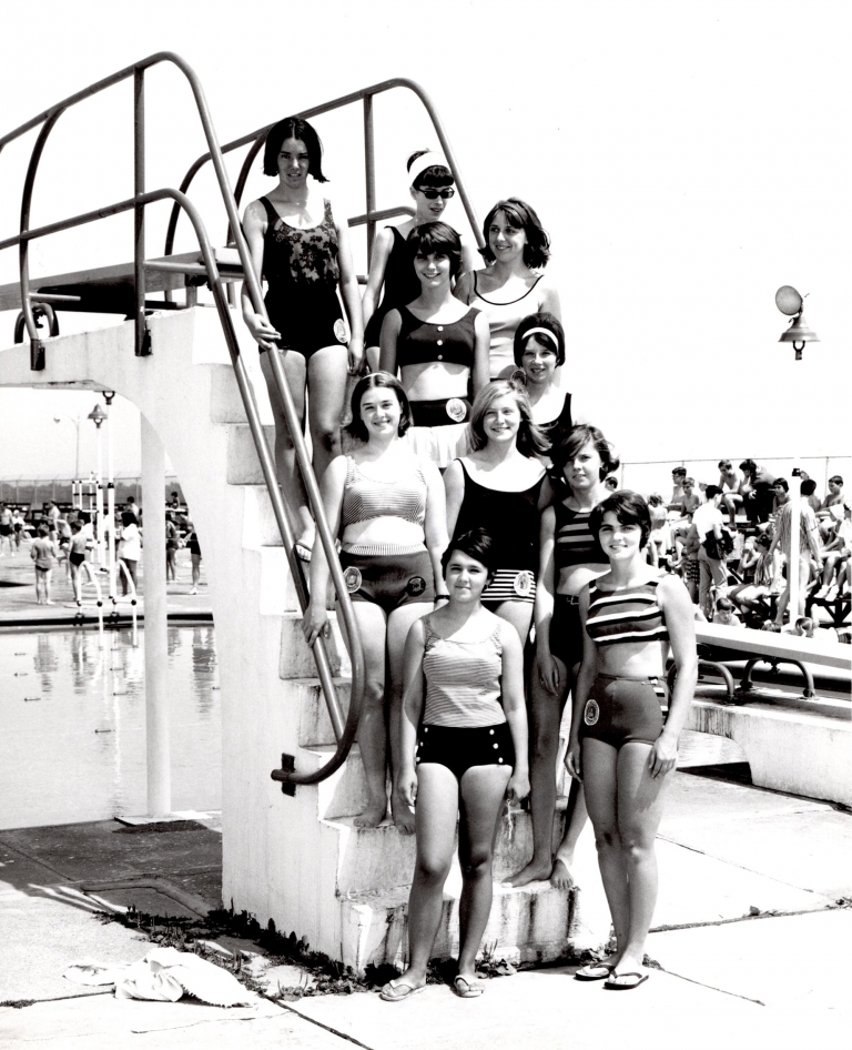 A group of female swimmers next to the diving board 